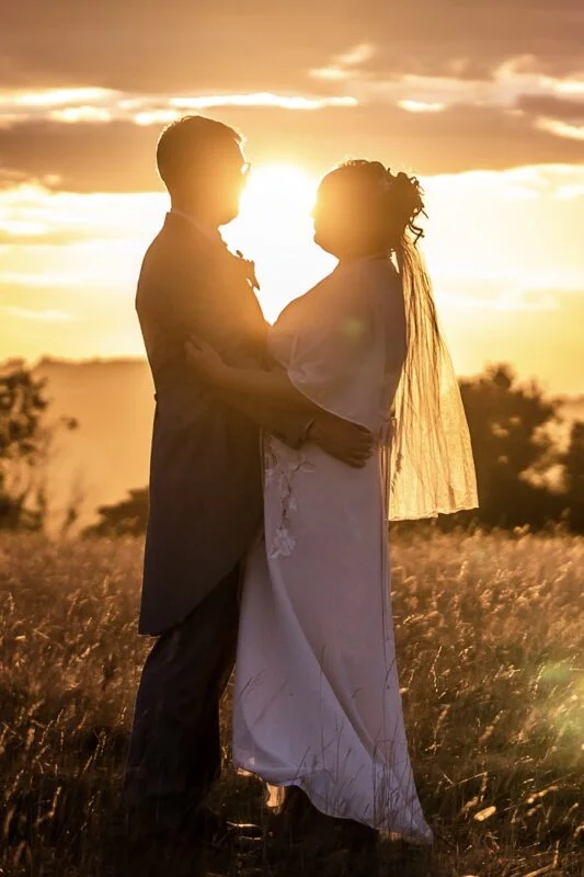 A bride and groom standing in a field at sunset.