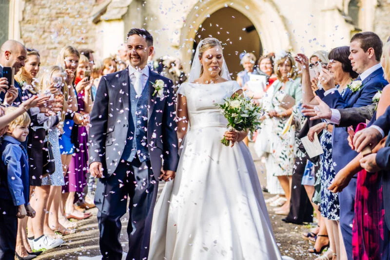The best wedding photographer in Bristol captures a bride and groom walking down the aisle with confetti.
