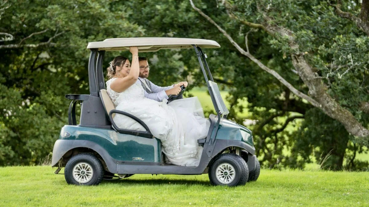 A bride and groom riding in a golf cart.