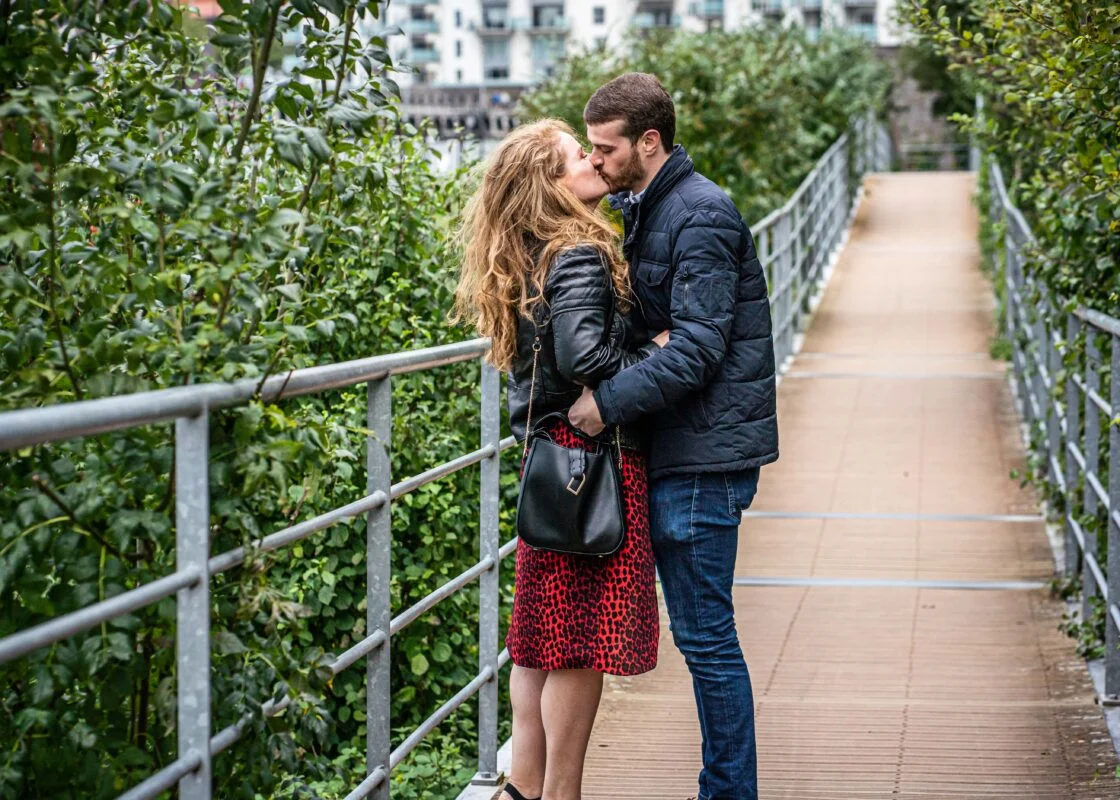 A couple kissing on a bridge in the city.
