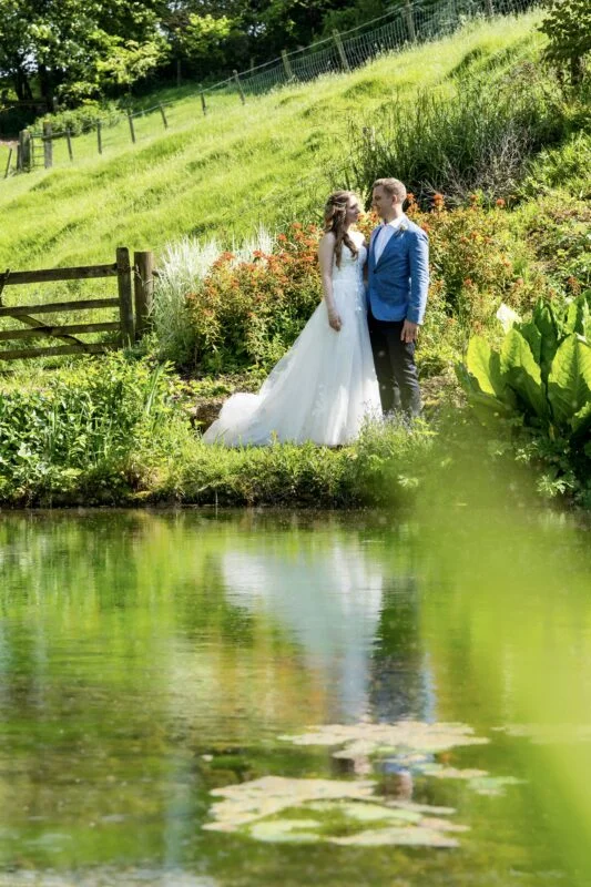 A bride and groom standing next to a pond.