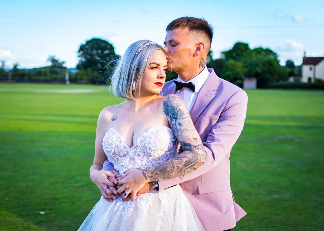 A bride and groom embracing in a field.
