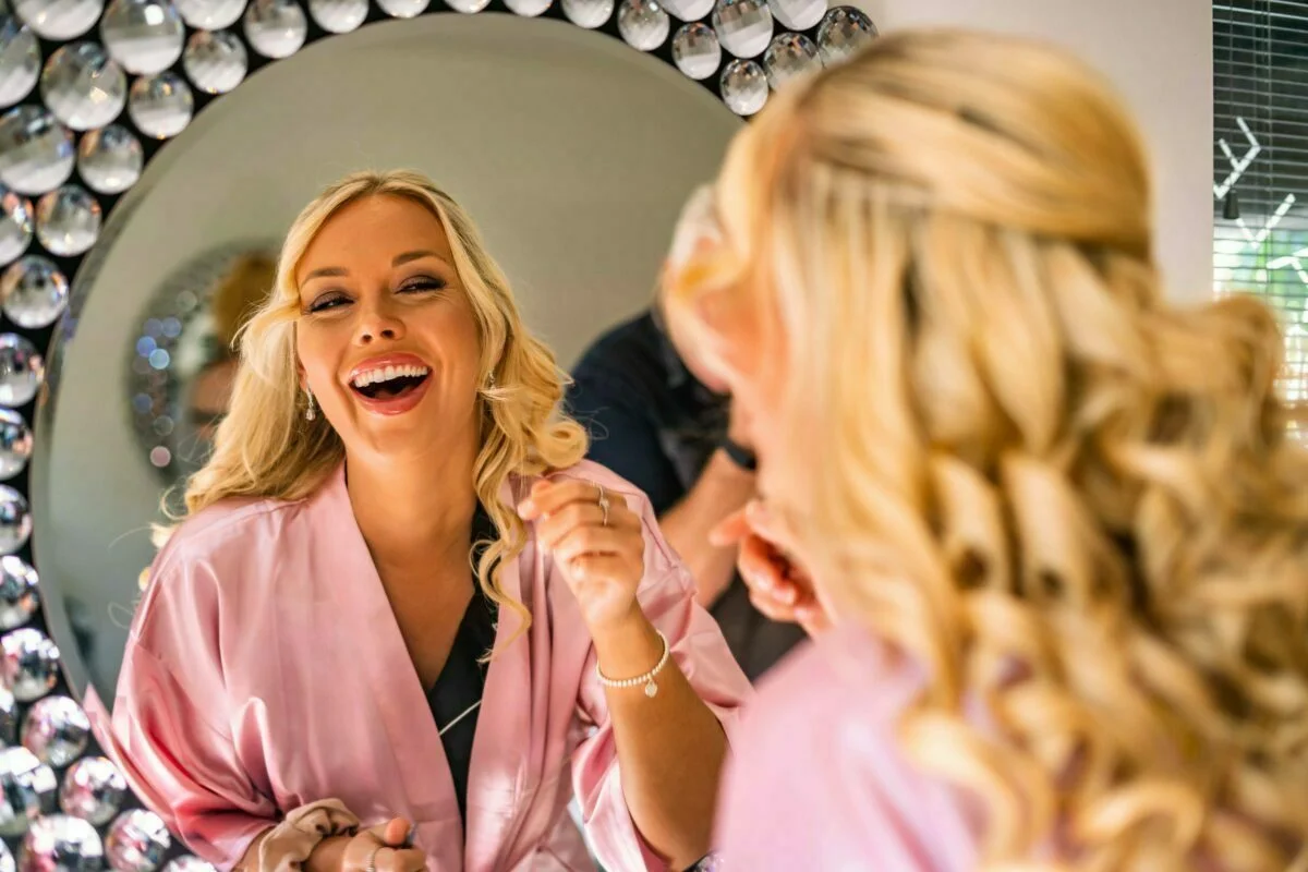 A woman in a pink robe laughing in front of a mirror.