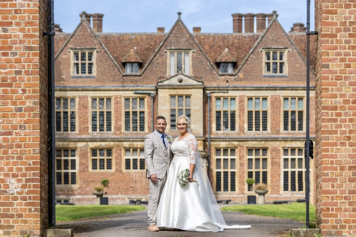 A bride and groom standing in front of a large brick building.