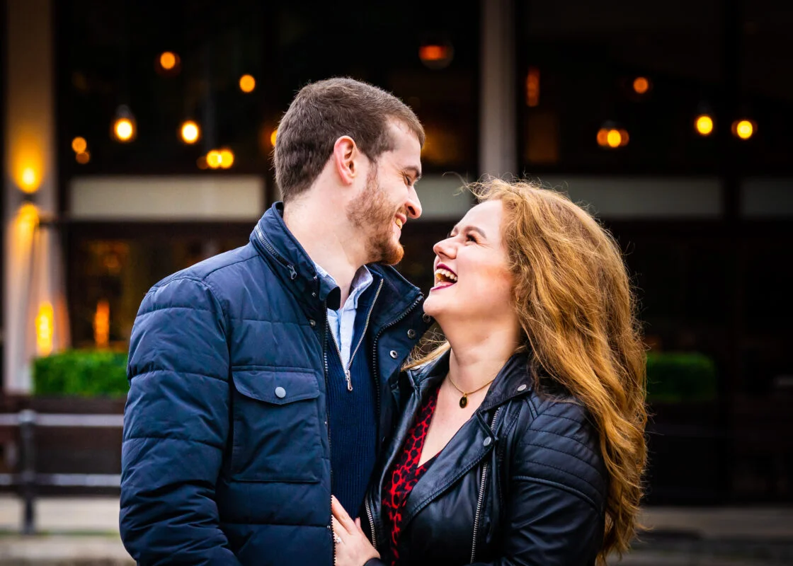 An engaged couple laughing in front of a building.