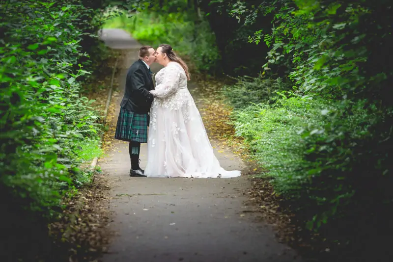 A bride and groom kissing on a path in the woods.