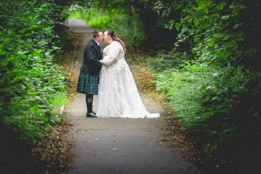 A bride and groom kissing on a path in the woods.