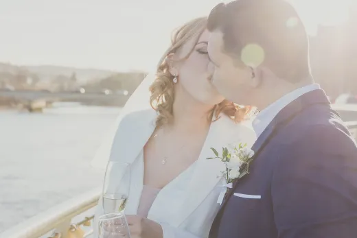 A bride and groom kiss in front of a river.