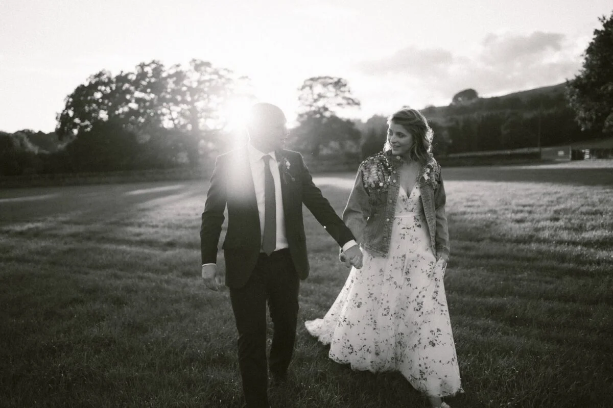 A bride and groom walking through a field at sunset.