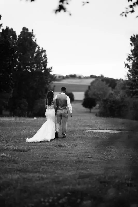 A bride and groom walking through a field in black and white.