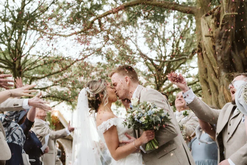 A bride and groom kissing in front of confetti.