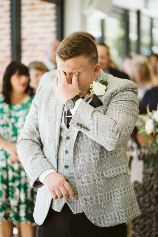 A man in a suit is wiping his face during a wedding ceremony.