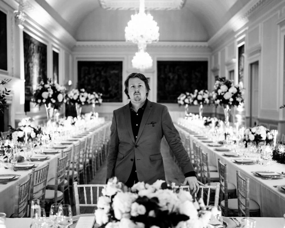 A black and white photo of a man standing in front of a long table.