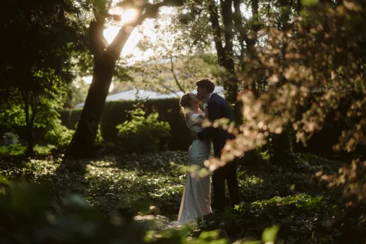 A bride and groom kissing in the woods.