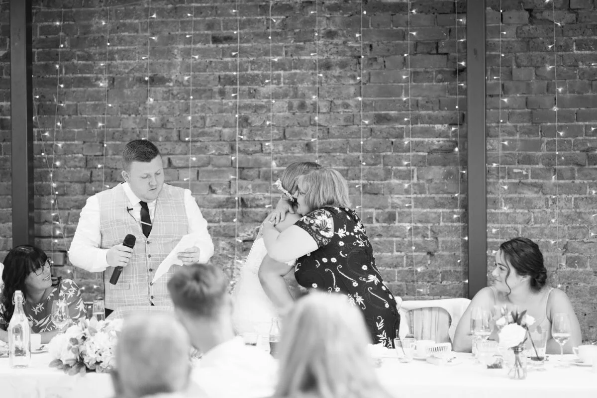 A black and white photo of a man giving a speech at a wedding.