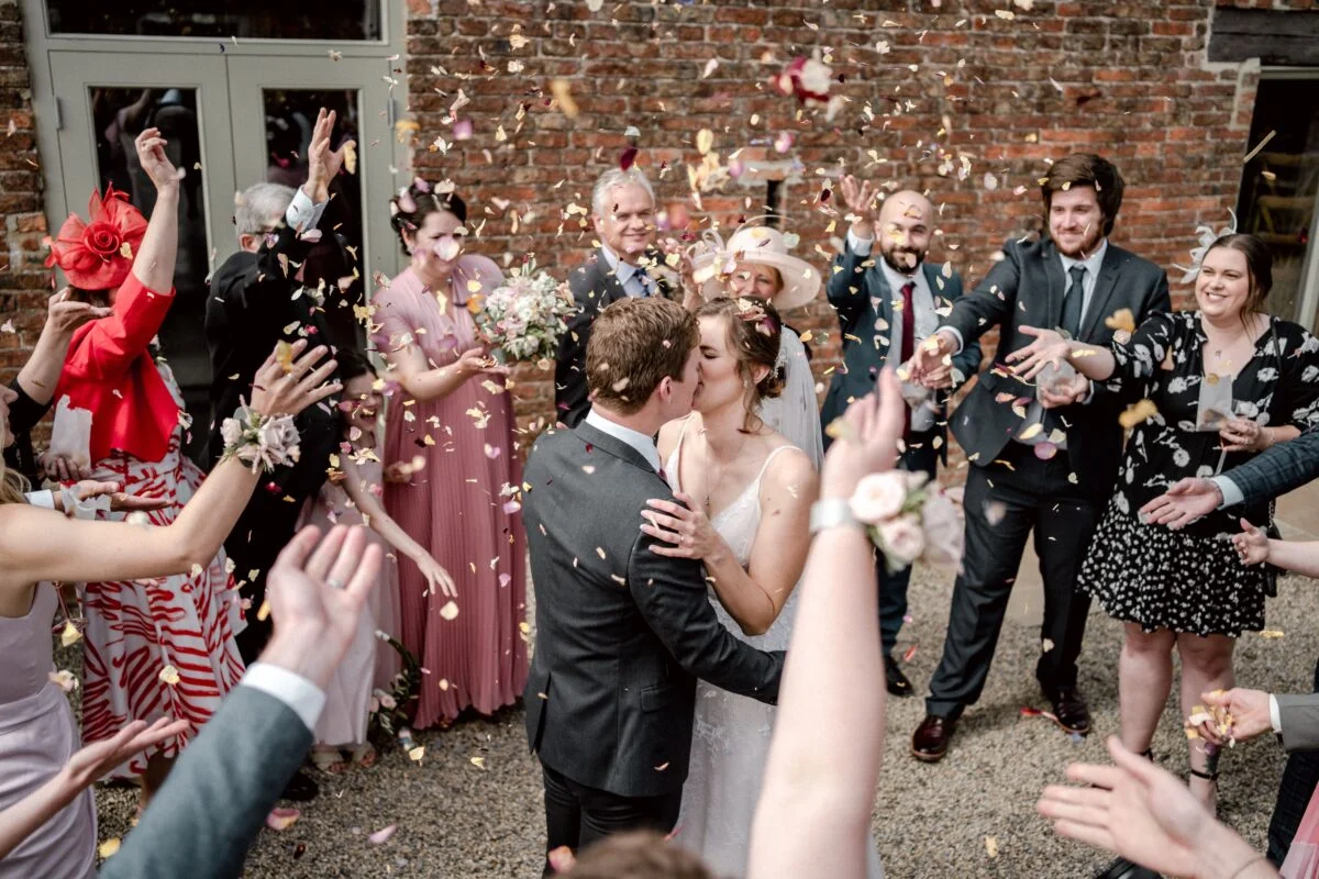 A bride and groom kissing in front of confetti.