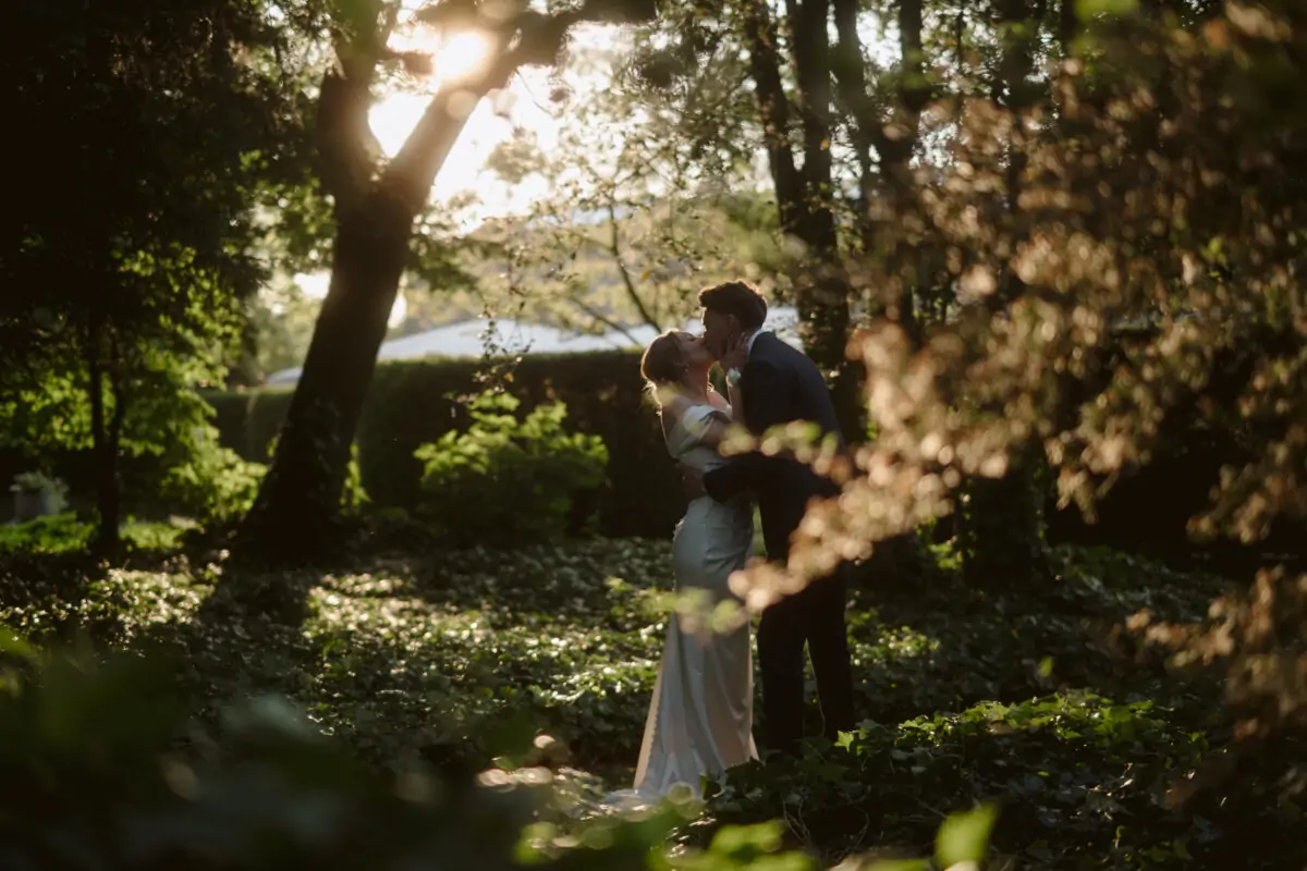 A bride and groom kissing in the woods.