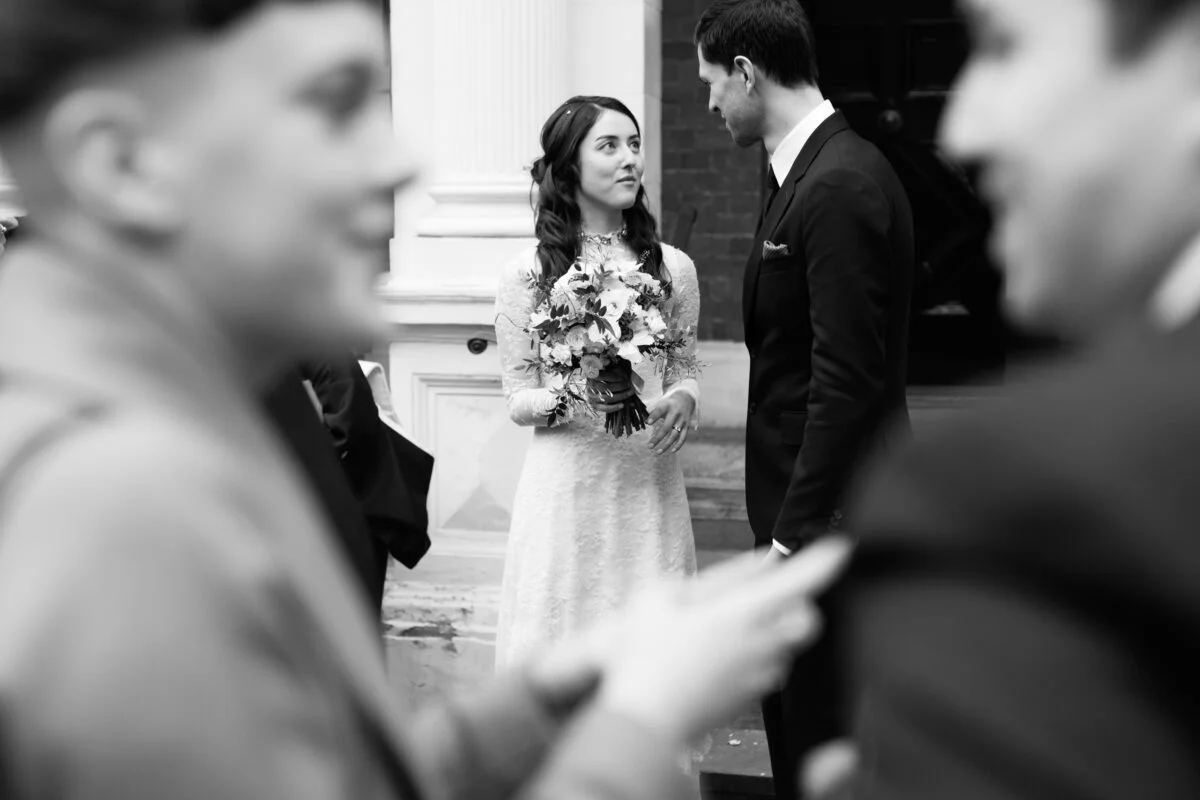 Black and white photo of a bride and groom in front of a church.