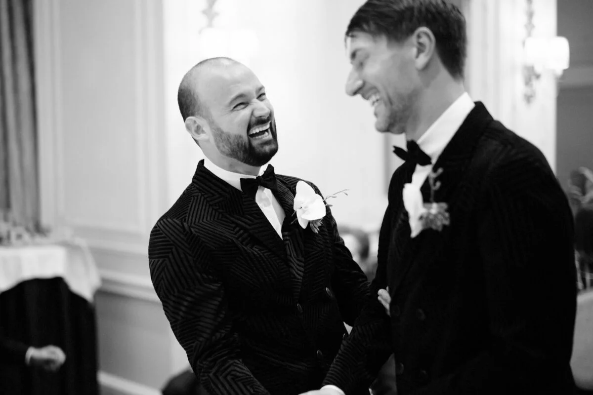 Two men in tuxedos smiling at each other.