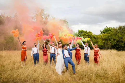 A group of bridesmaids and groomsmen in a field with colored powder.