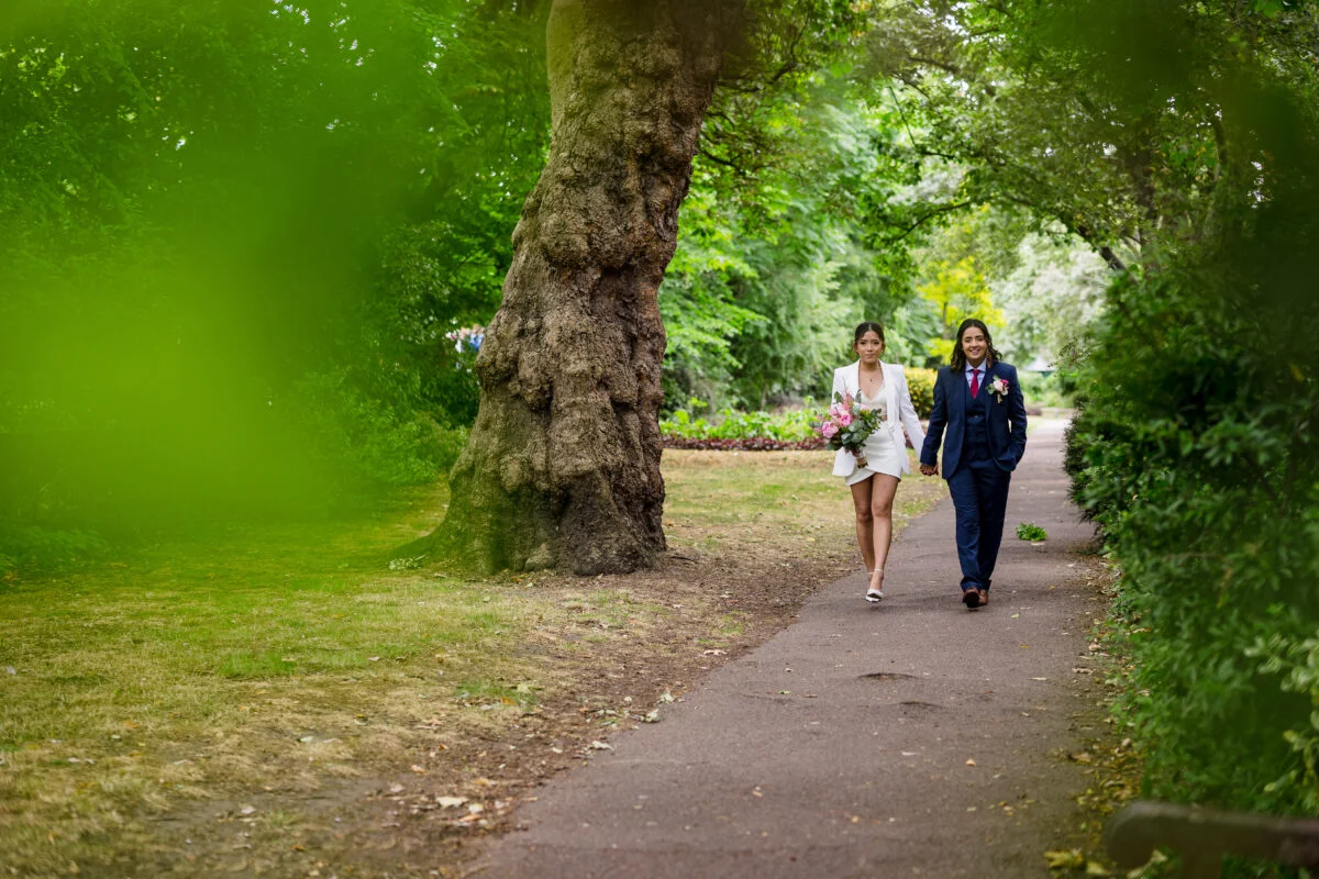 A bride and groom walking down a path in a park.