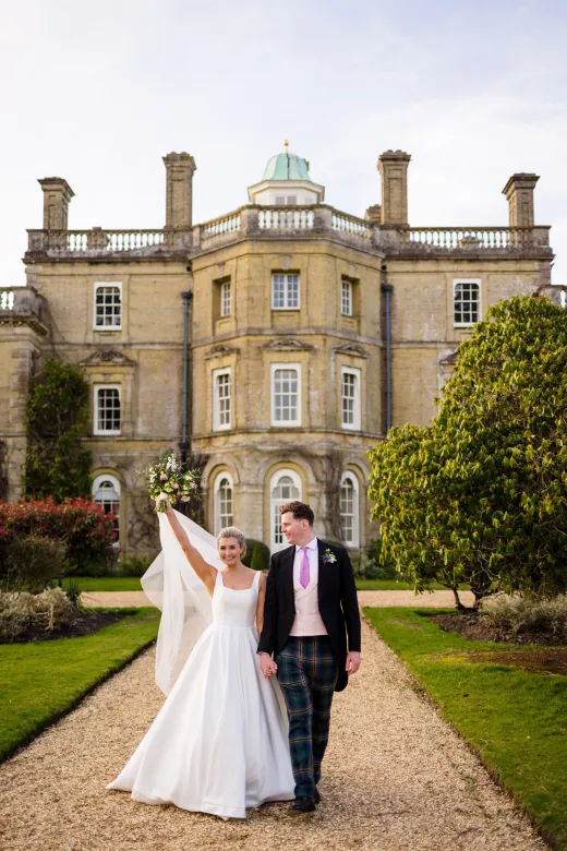 A bride and groom standing in front of a large mansion.
