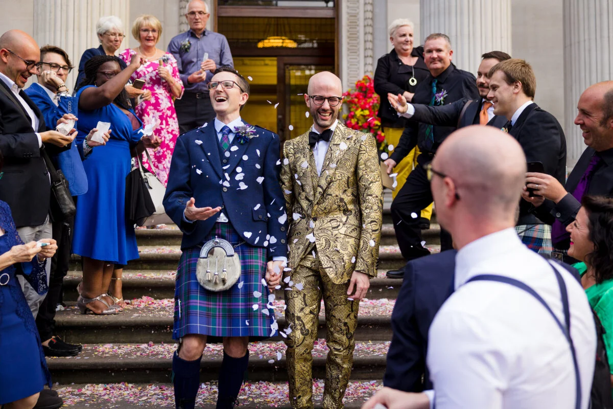 A group of men in suits and kilts are throwing confetti at each other.