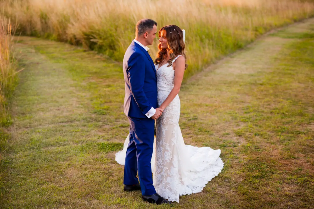 A bride and groom standing in a field with tall grass.