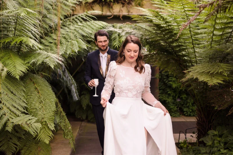 A bride and groom walking through a greenhouse.