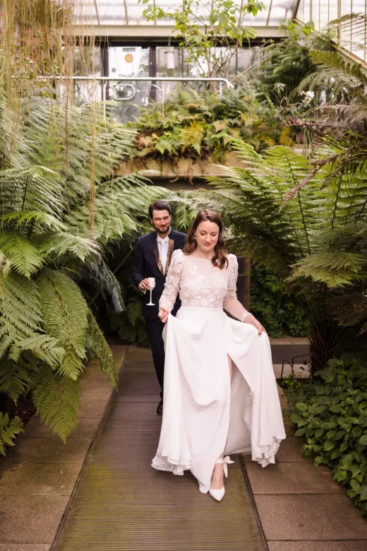 A bride and groom walking through a greenhouse.