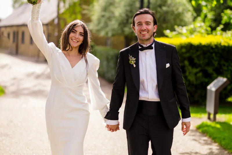 A bride and groom holding hands walking down a path.