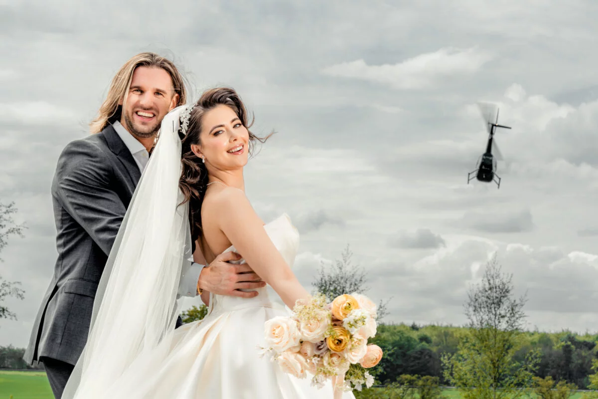 A bride and groom posing in front of a helicopter.