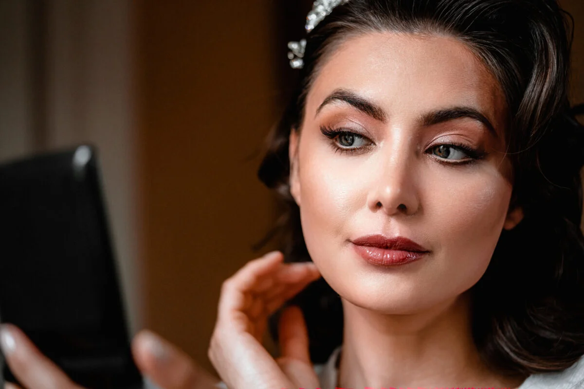 A woman is looking at her makeup in a mirror.
