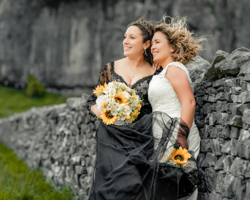 Two brides leaning against a stone wall.
