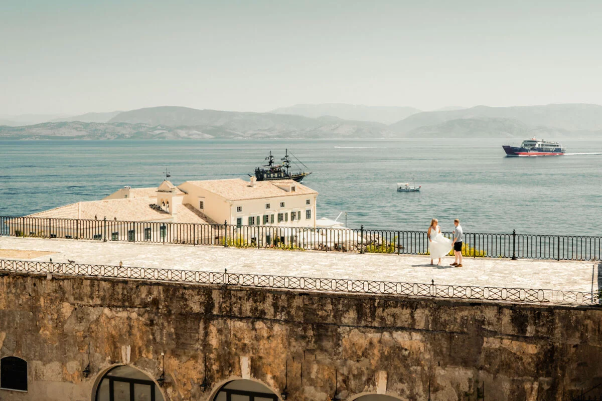 A bride and groom standing on a rooftop overlooking the sea.