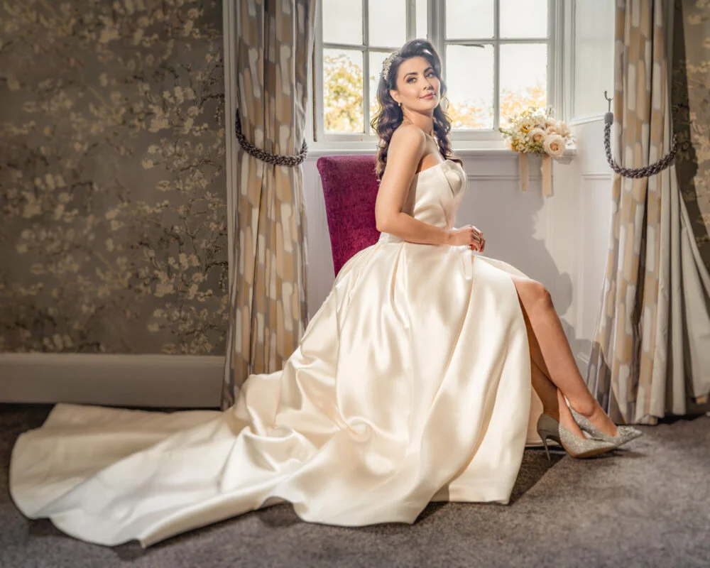 A bride in a wedding dress posing in front of a window.