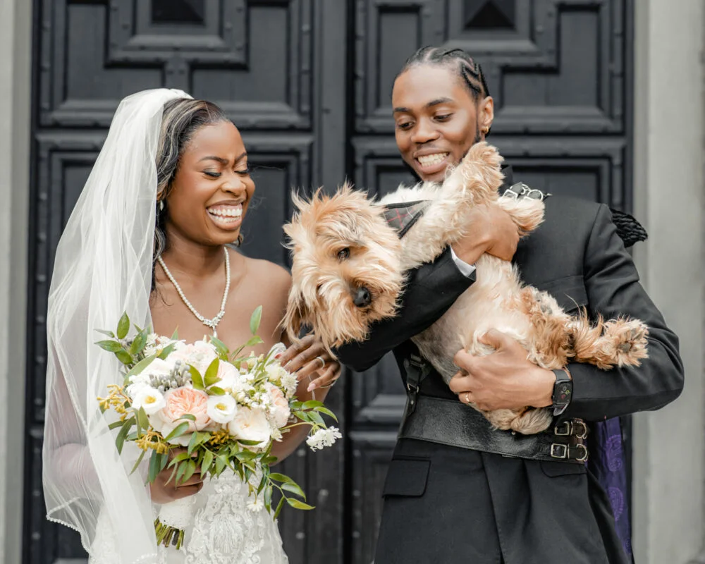 A bride and groom with a dog in front of a door.