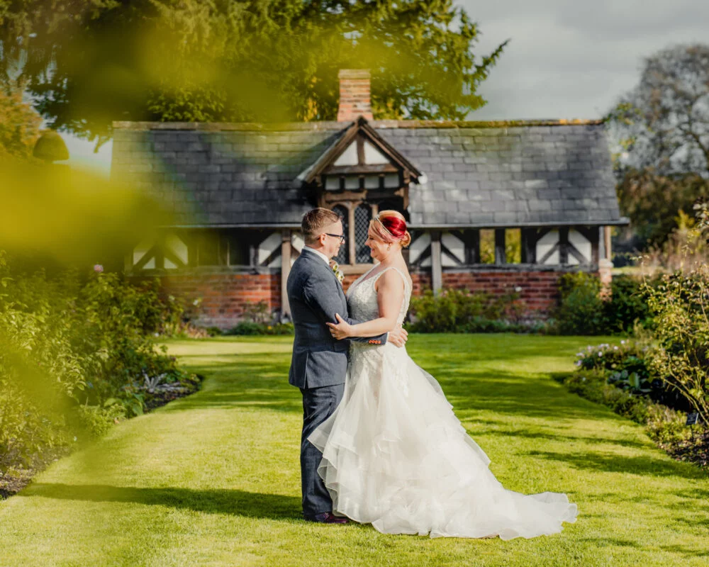 A bride and groom standing in front of a cottage.