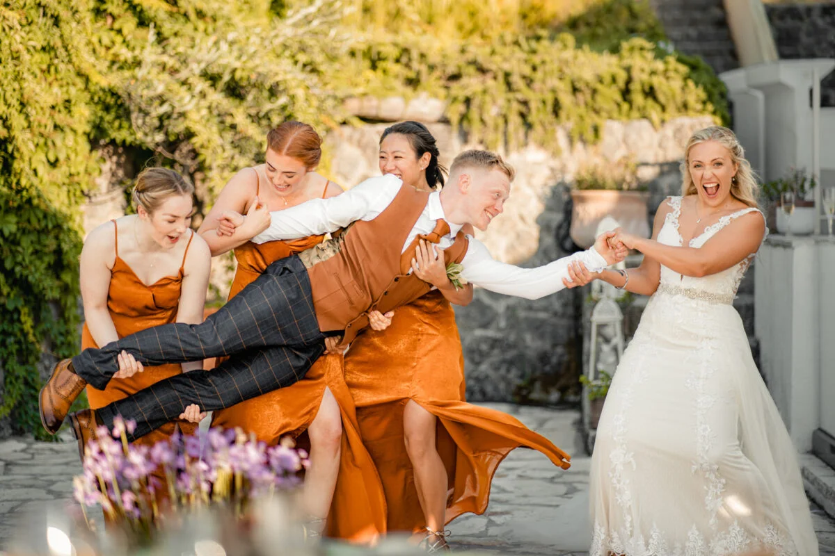 A group of bridesmaids playing with a man in an orange dress.