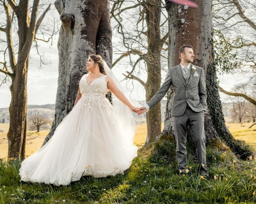 A bride and groom holding hands in a field of trees.