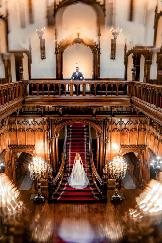 A bride and groom standing on a staircase in an ornate building.