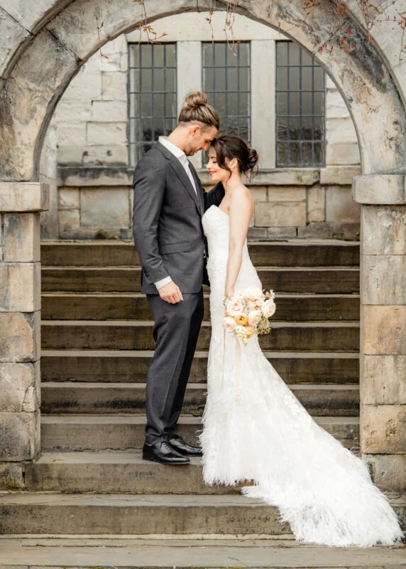 A bride and groom standing on steps in front of an archway.