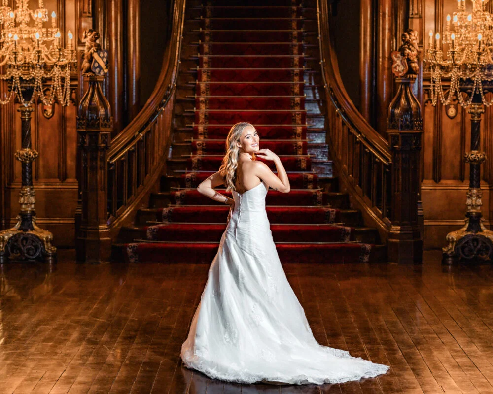 A bride posing in front of a staircase in an ornate building.