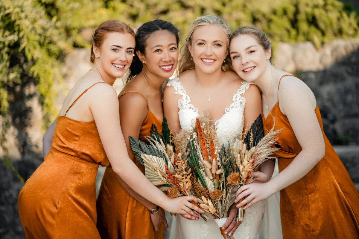 Four bridesmaids in orange dresses posing for a photo.