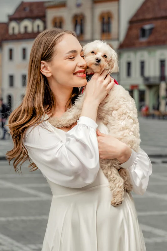 A pregnant woman with a white dress holding a small white dog.