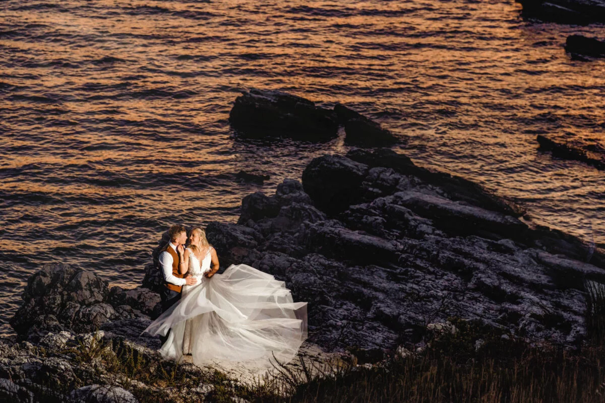 A bride and groom standing on a cliff overlooking the ocean.