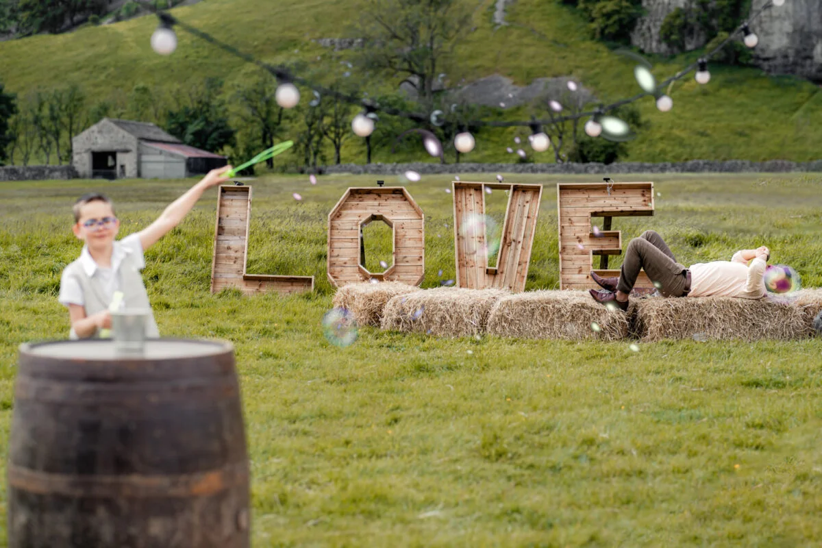 A man blowing bubbles in front of a love sign in a field.
