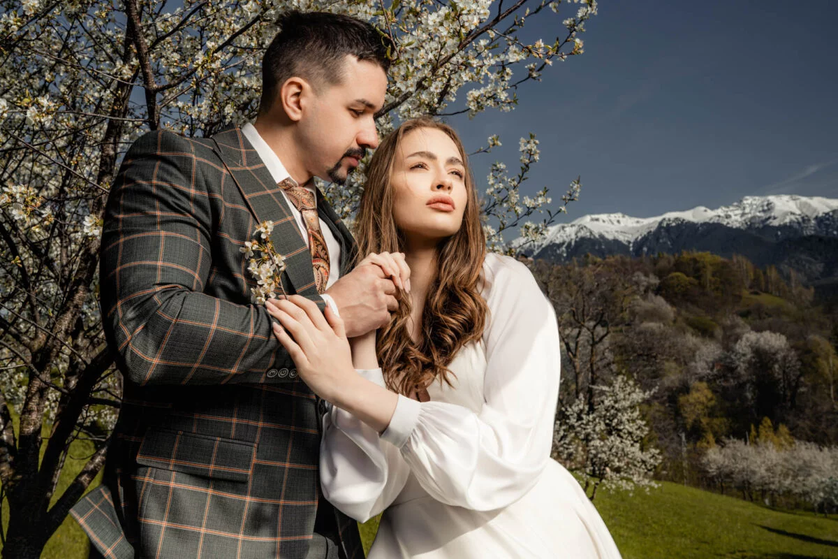 A bride and groom posing in front of a flowering tree.