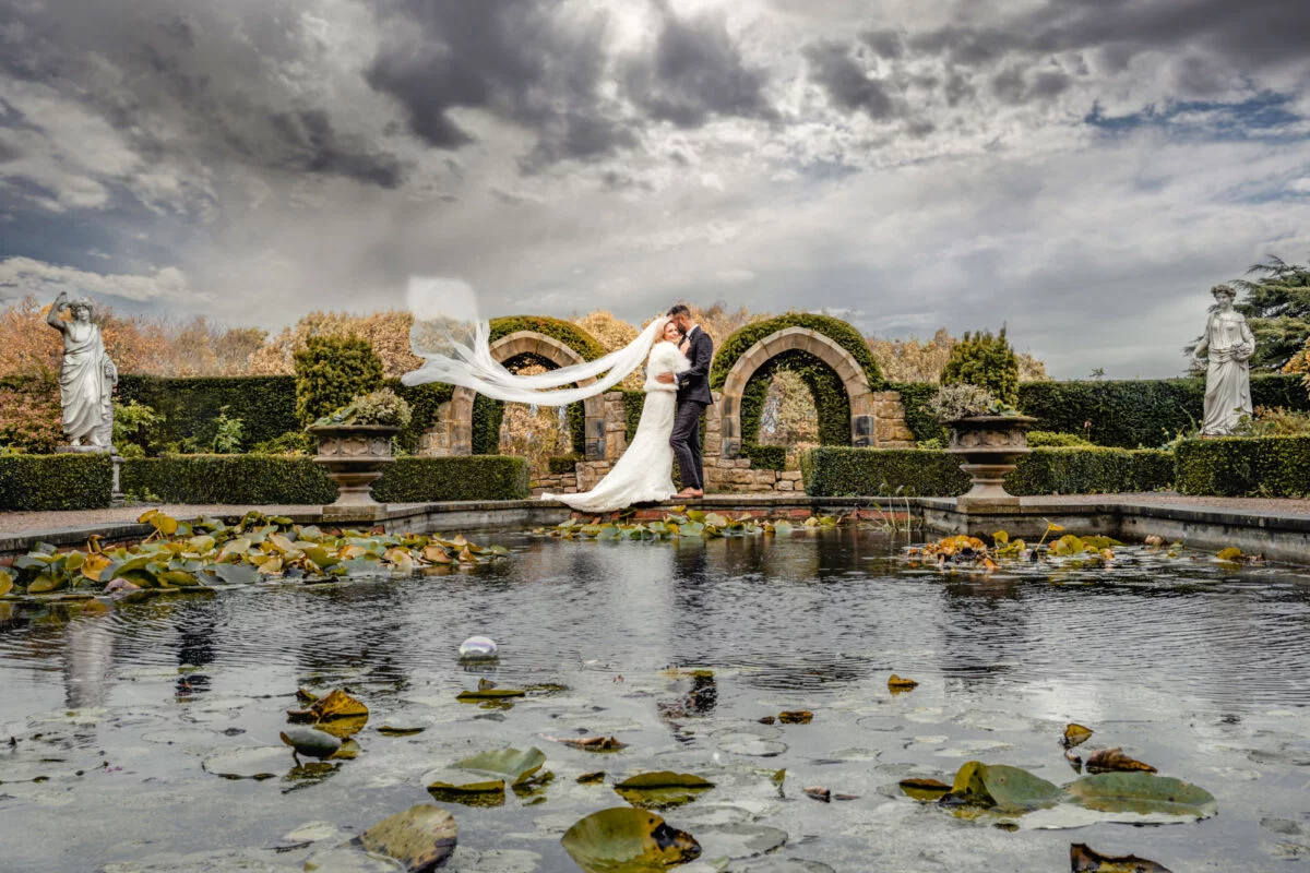 A bride and groom standing in front of a pond.