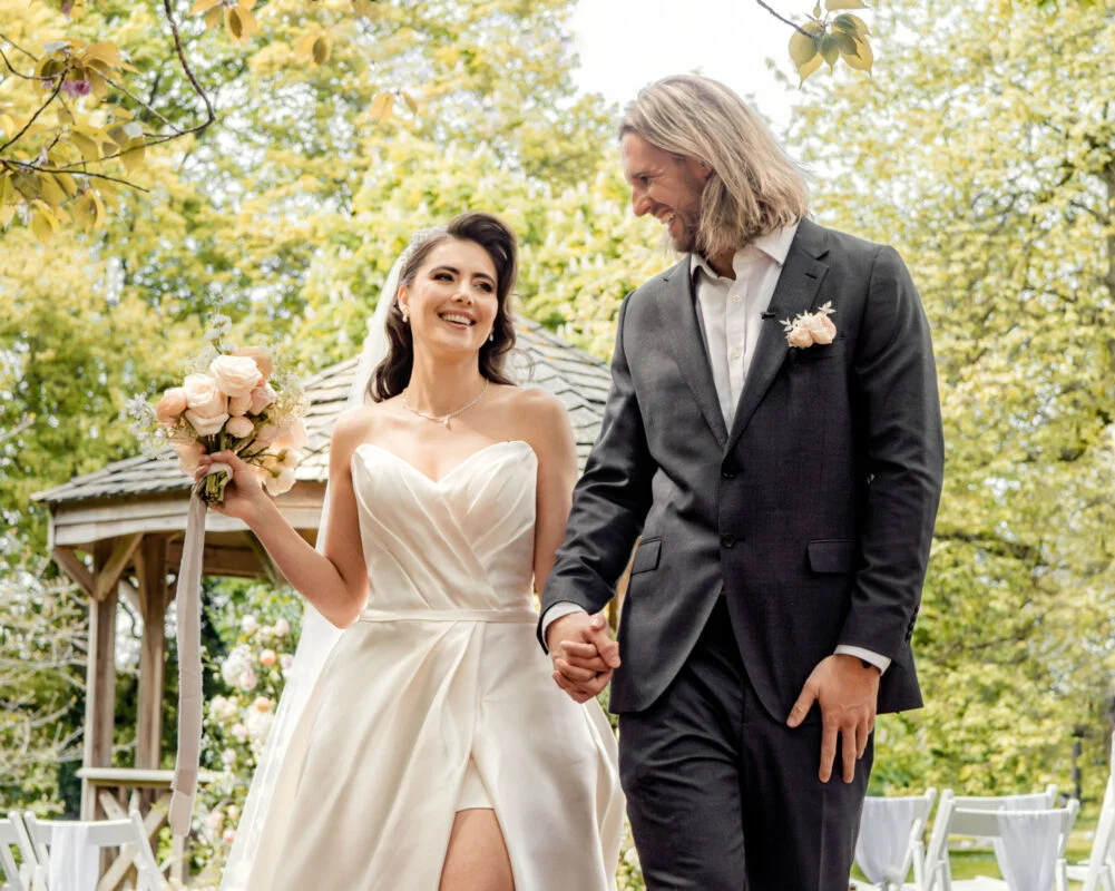 A bride and groom holding hands in a park.